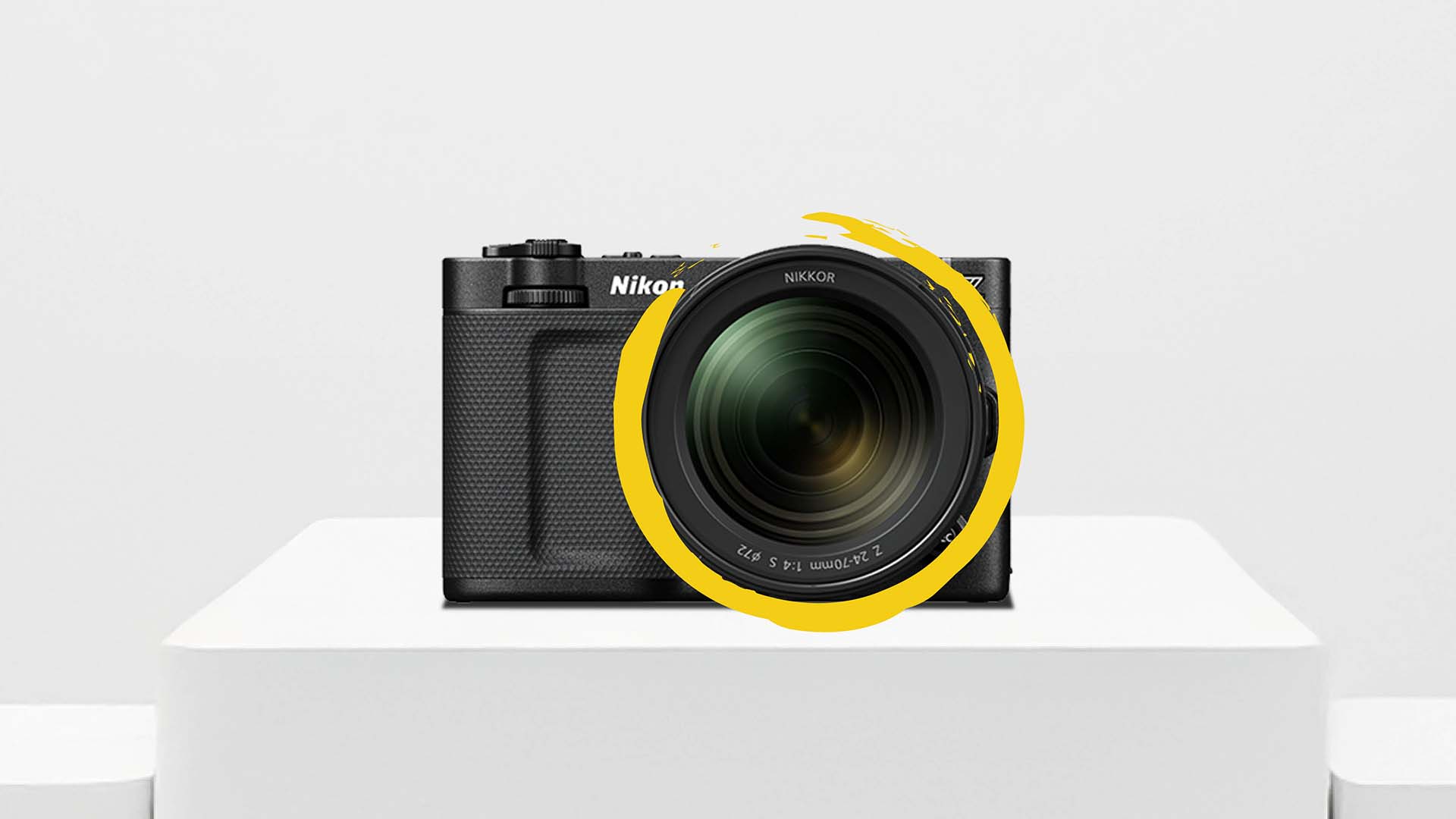 Front view of the Nikon ZR cinema camera with attached NIKKOR lens, displayed on a white pedestal with a yellow graphic accent.