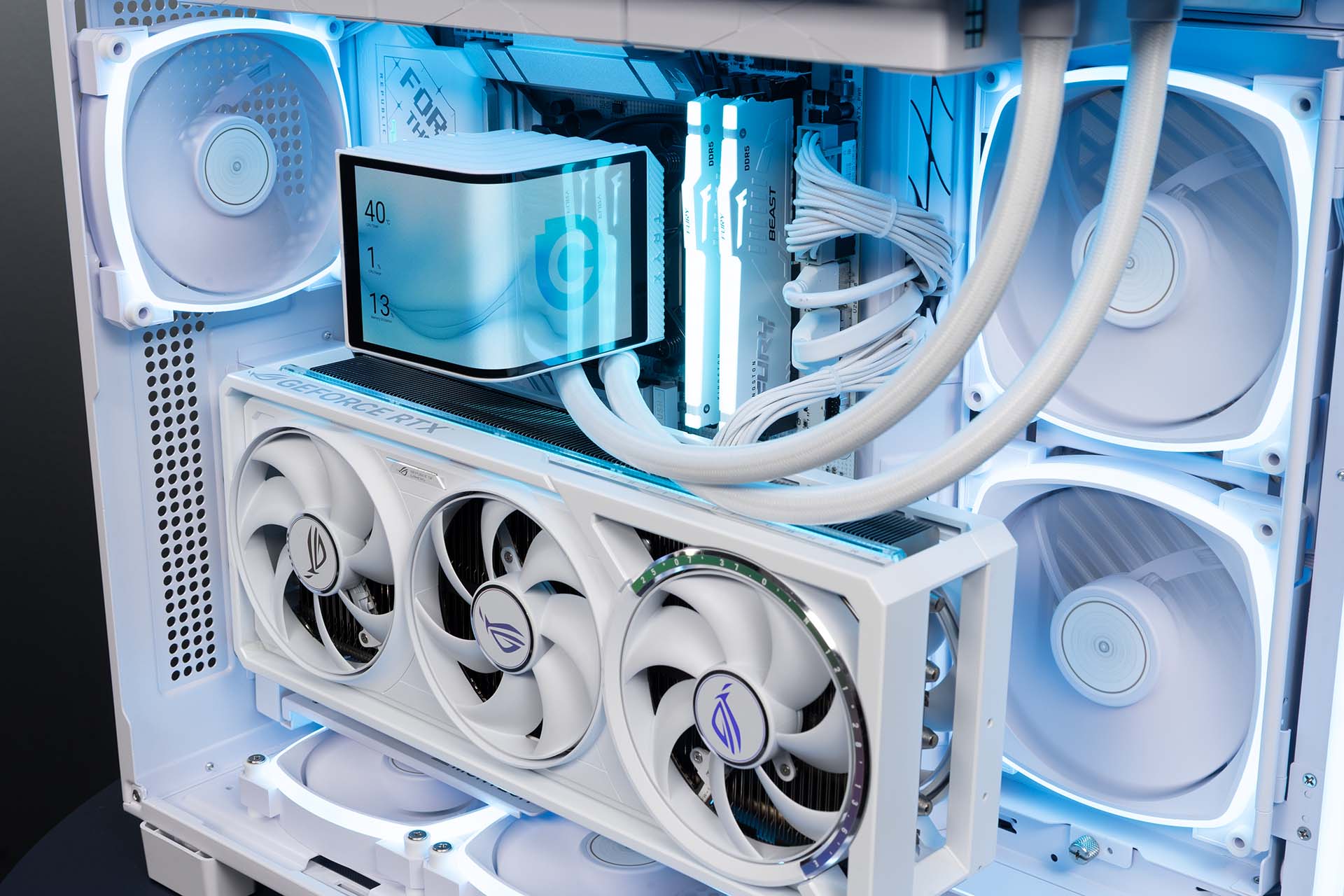 Close-up of the Chillblast Glacienne white gaming PC interior, featuring RGB-lit cooling fans, custom liquid cooling, white cabling, GeForce RTX graphics card, and illuminated RAM.