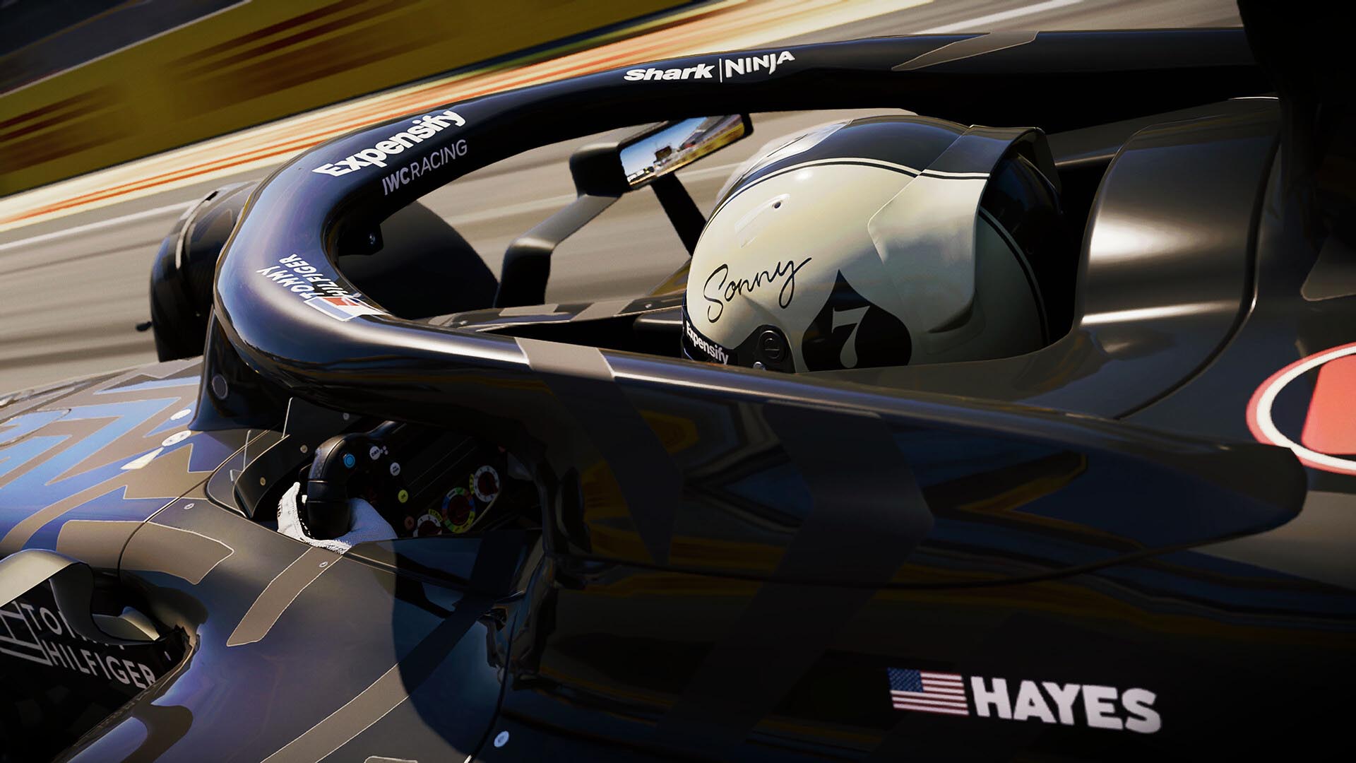 Close-up of a Formula 1 driver named "Hayes" in an APXGP car from F1 25, featuring a custom helmet marked "Sonny" and a stylized spade graphic, captured during high-speed gameplay on a racetrack.