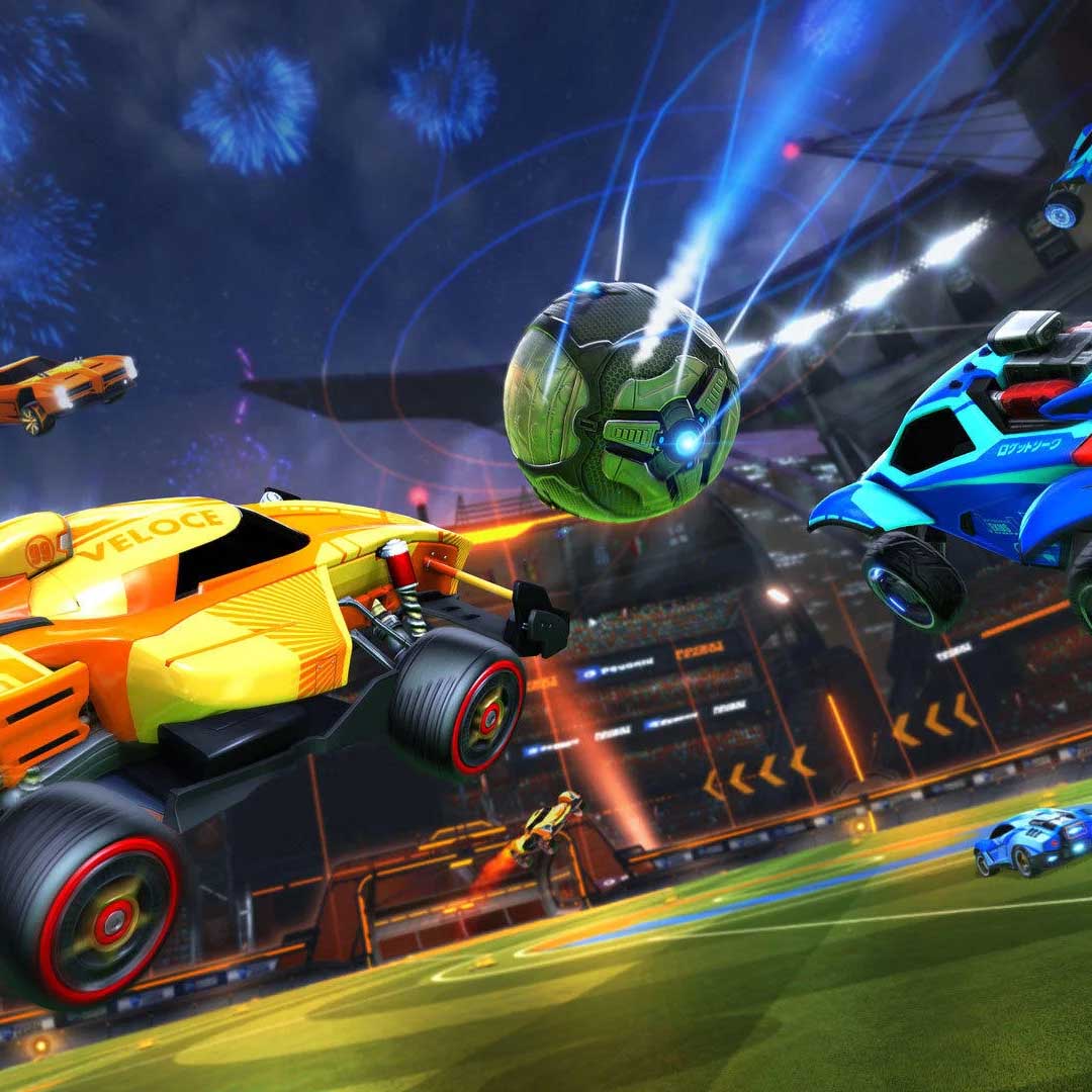 In-game screenshot from Rocket League showing brightly colored rocket-powered cars mid-air as they chase a glowing soccer ball in a futuristic stadium, with fireworks in the background.