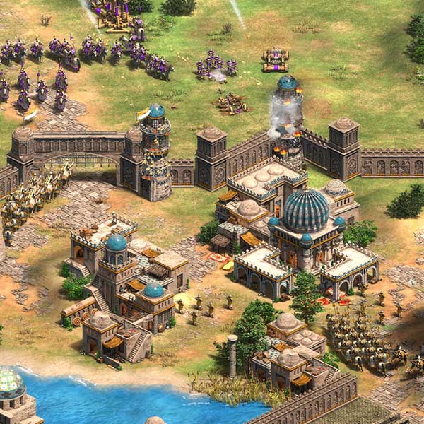 In-game screenshot from Age of Empires II: Definitive Edition showing a detailed medieval city under siege, with walls, burning towers, and armies clashing near a waterfront.